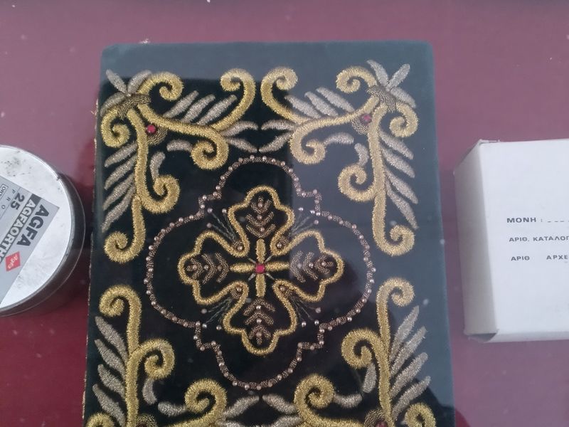 Σταυρός και φυτικά μοτίβα με χρυσαφί και ασημί κέντημα, χάντρες και κόκκινα διακοσμητικά στοιχεία σε σκούρο ύφασμα.